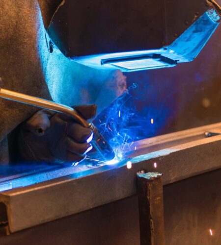 Young man with protective mask welding in a factory