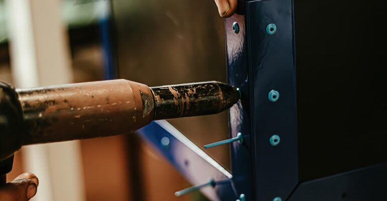 Male worker uses electric riveting gun. Hand holding  riveting machine and placing rivets. Working workshop of carpenter or mechanic.