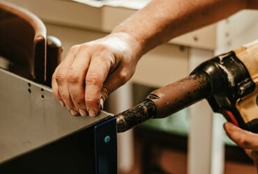 Male worker uses electric riveting gun. Hand holding riveting machine and placing rivets. Working workshop of carpenter or mechanic.